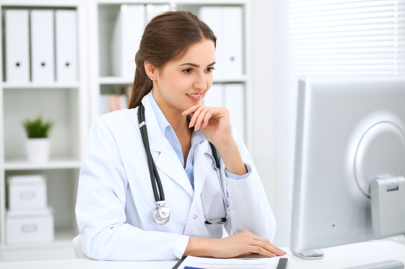 Ärztin sitzt an ihrem Schreibtisch und blickt interessiert auf Ihren Computerbildschirm